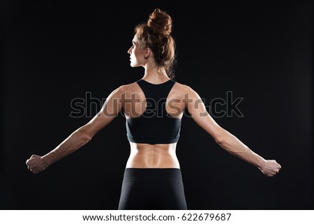 Back view image of young sports lady standing over black background and posing. Looking aside.