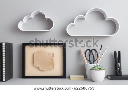 Blank picture frame or poster, office supplies, books and plant on a gray wall.
