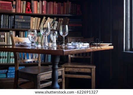 Table set for two with wine glasses by window with books in the background. Intimate, private, cozy feeling.