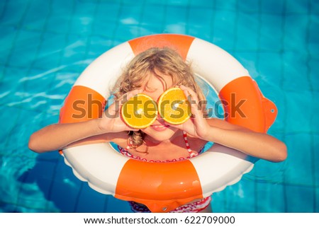 Child with orange outdoor. Kid having fun in swimming pool. Summer vacation and healthy eating concept