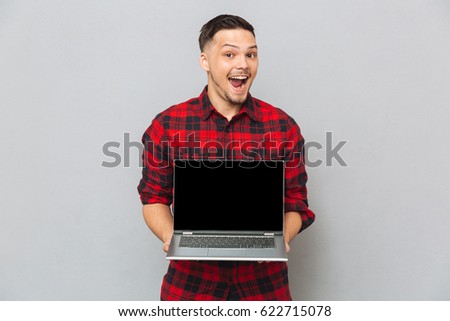 Happy man in red shirt showing laptop computer screen at the camera over gray background