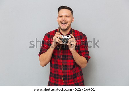 Happy Man in shirt making photo on retro camera over gray background