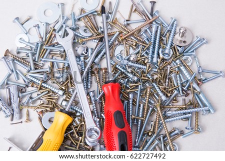 Phillips and flat screwdriver with magnetic tips over the set of screws, bolts, dowels and wrench on the table. Fasteners and hand tools.