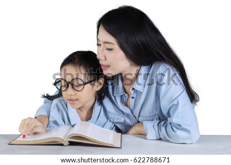 Photo of a young Asian woman teaching her daughter to read a book on the table, isolated on white background