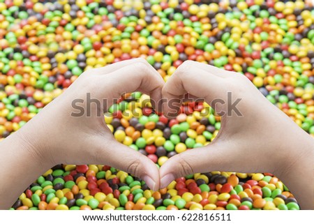 Close up of hands of child make a heart symbol with colorful candies background
