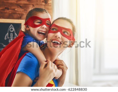 Mother and her child playing together. Girl and mom in Superhero costume. Mum and kid having fun, smiling and hugging. Family holiday and togetherness.
