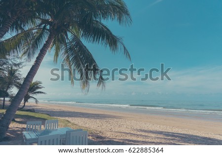 vintage tone image of wood table under coconut tree  and blue sea and cloudy sky in background.