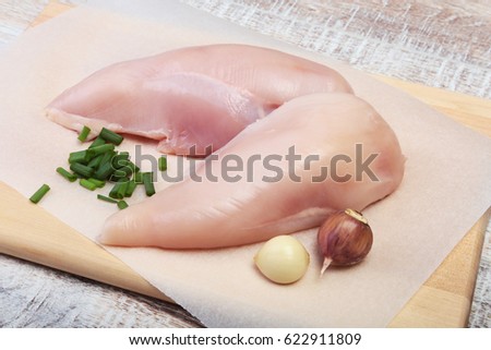 Raw chicken breast fillets and garlic ready for cooking on wooden board