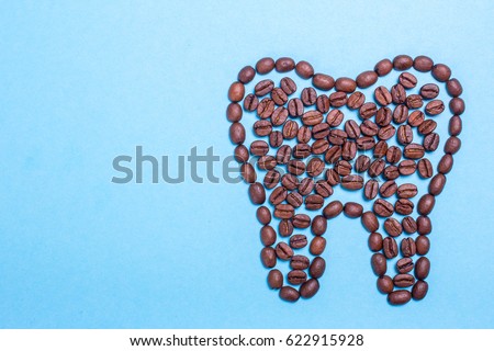 Unhealthy yellow teeth from coffee. Tooth from coffee beans on a blue background