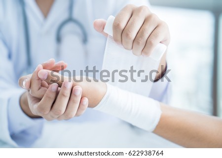 Close-up doctor is bandaging upper limb of patient. Royalty-Free Stock Photo #622938764