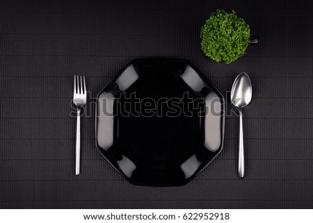 Dark modern minimalistic restaurant menu mock up  with black glossy plate, spoon, fork and green plant, top view.