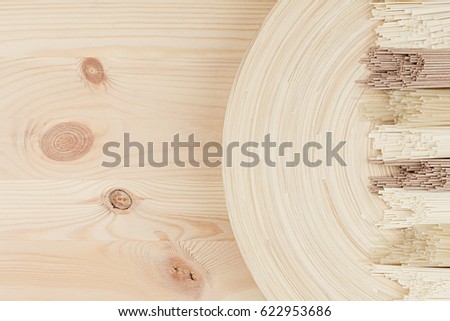 Raw asian noodles on beige wooden dish on white board, top view. Decorative border with copy space.