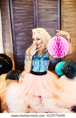Beautiful young girl with long curly blond hair. A girl in an airy tutu with colorful multicolored balloons and pompoms