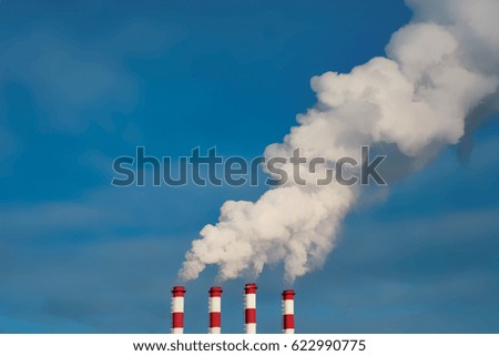 Blue sky and four smokestacks of a thermal power station with clouds of smoke, air steam in a winter day.