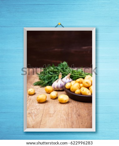 Potatoes in plate. Carrot tops, garlic and raw new potato. Fresh natural vegetables. Organic bio food on rustic wooden table. Photo frame on wooden rustic wall.