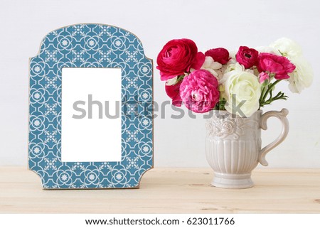 Image of beautiful bouquet of spring flowers next to blank vintage photo frame on wooden table. For photography mock up montage