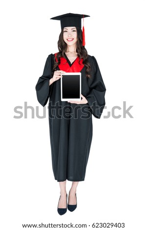 Beautiful young brunette woman in mortarboard holding digital tablet and smiling