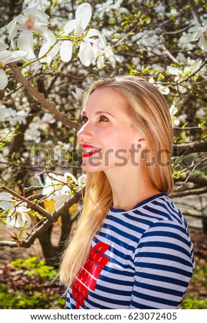 Portrait of spring blonde girl standing outdoor in blooming magnolia garden