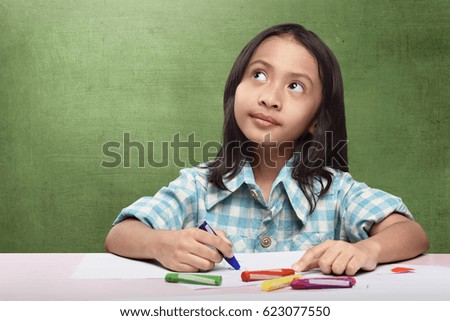 Cheerful asian child imagining something to drawing with crayon at school
