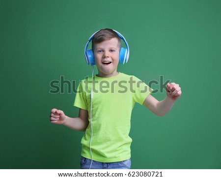 Cute little boy in headphones listening to music on color background
