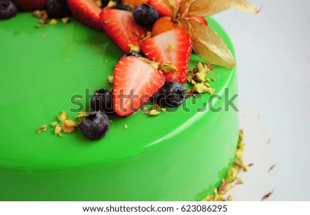 Modern French mousse cake with green mirror glaze and with berries, pistachios. Close-up. Picture for a menu or a confectionery catalog.