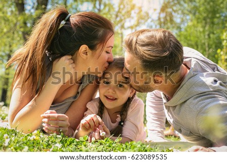 Parents kissing her daughter lying on the meadow.
