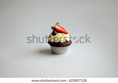 Chocolate cupcake with whipped vanilla cream, fresh strawberry, blueberry on gray background. Picture for a menu or a confectionery catalog.