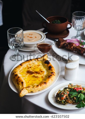 Beautiful Georgian cuisine on a white tablecloth: huge glossy khachapuri with suluguni cheese and shiny egg, chicken sacivi in a white plate, lobio and sashlik on a background. Vertical photo