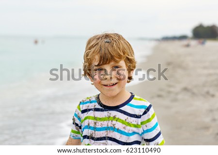 Adorable active little kid boy having fun on beach of Denmark, North Sea. Happy cute child relaxing, playing and enjoying stormy warm day near palms and ocean. Kid with sand on funny beautiful face