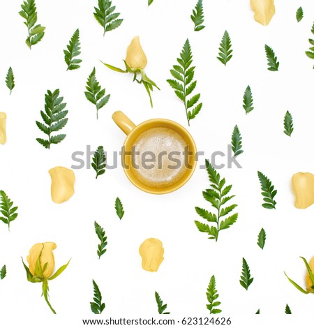 Floral pattern with green leaves, yellow rose petals and a cup of coffee on white background. Flat lay, top view.