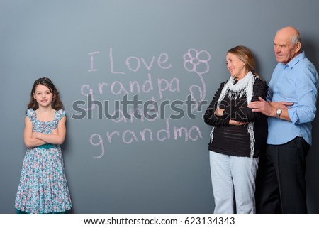 Pink hand-drawn text and a flower on the gray wall. Love expression of little girl. Grandparents look at their grandchild tenderness and appreciate her confession.