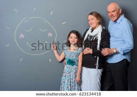 Lovely family beside chalk picture. Sun depicted on the girl's drawing and family's mood is sunny. Nice studio shot with gray wall background.