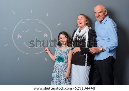 Family in a lifted mood. Lovely shot of happy relatives beside the girl's painting of smiling sun. Horizontal photo with gray background.