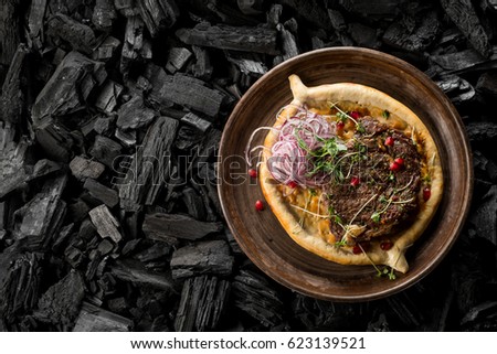 Fried barbecue meat with garnish - vegetables, spices and sauce on a bread plate. Traditional Georgian cuisine, restaurant menu. Food photo with text area for design. Dark background. Flat, overhead.