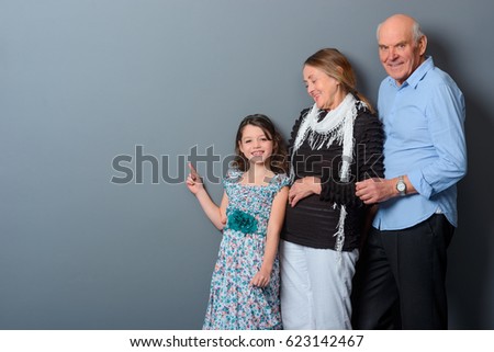 Happy old couple with young girl. Granddaughter show with a point finger on the empty space for your text or picture.