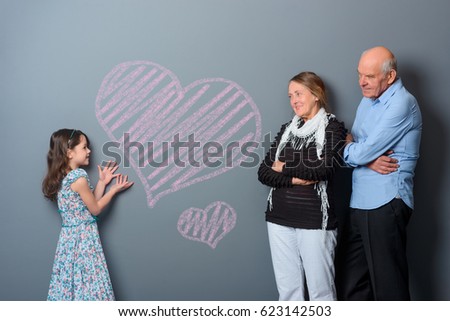 Hearts depicted by a young girl. Granddaughter shows her love to grandparents using her picture of hearts. Tender glance of two old people.