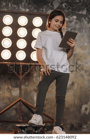 Little girl with skateboard and tablet in loft appartment