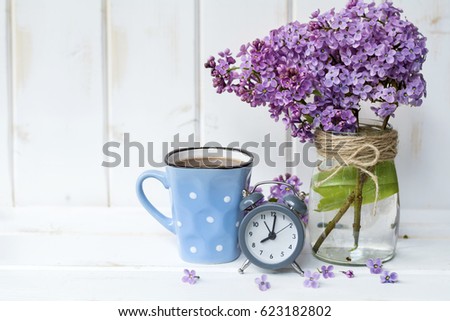 Bouquet of lilac  with alarm clock on white  wooden background.Morning energy concept