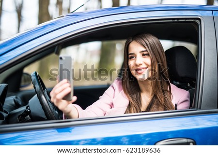 Smiling woman taking selfie picture with smart phone camera outdoors in car