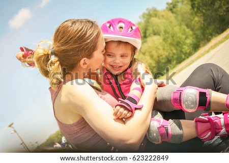 Mother and daughter resting on a bench after skating and enjoying in beautiful day.  Mother kissing her little daughter.