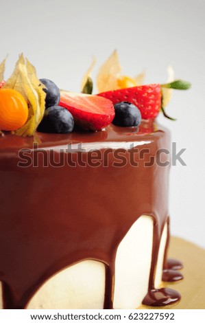 Vanilla cake in chocolate with strawberries, blueberries and physalis. Close-up. Picture for a menu or a confectionery catalog.