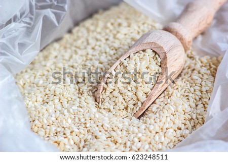 Macro photo of organic natural white sesame seeds on wooden spoon in white plastic shopping bag close up. Natural light. Selective focus. Shallow DOF 