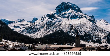View of Lech am Arlberg in Austria on a beautiful Spring day, showing the buildings of the town and surrounding snowy mountains.