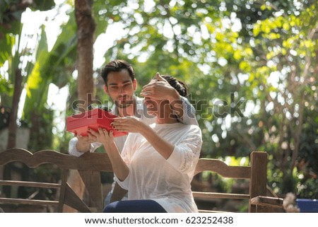 Selective focus at red box. happy business family couple surprising each other with red box presents. Husband closing eyes of his excited wife. cozy moments in summer holidays in the backyard.