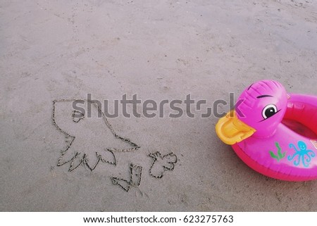 Children draw squid on the beach with a pink duck life ring put on the side.