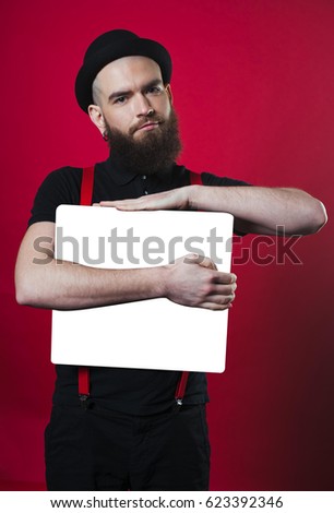 Funny man with a beard. The guy is holding a white sheet in his hands. Bearded guy on a red background. Cheerful bearded man. Bearded guy holding empty paper