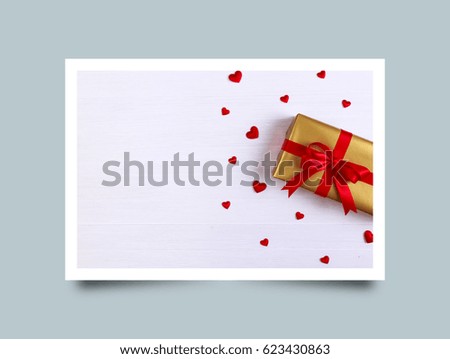 Gift box with red satin hearts. Present wrapped with ribbon and bow. Christmas or birthday golden paper package. On white wooden table. Photo frame design with shadow.