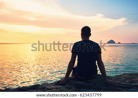 Contemplation at the beautiful sunset. Silhouette of the young man on the beach.  Royalty-Free Stock Photo #623437799