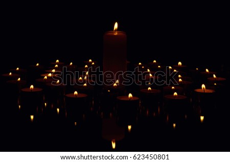 Many burning candles with reflection on dark background.