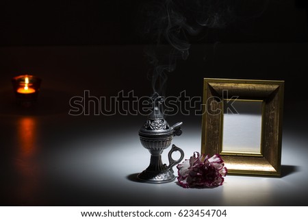 blank gilded picture frame with thurible and candle flame and carnation on dark 